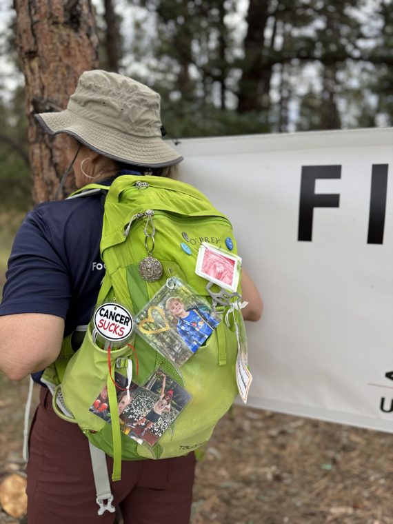 A hiker wearing a backpack covered in CureSearch pins