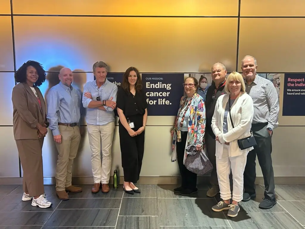Supporters and CureSearch staff gather in front of the CureSearch mission wall during a lab tour