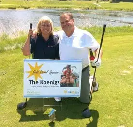 Harry and Robin Koenigs stand behind their Jakefest gold-level sponsor sign on the golf course