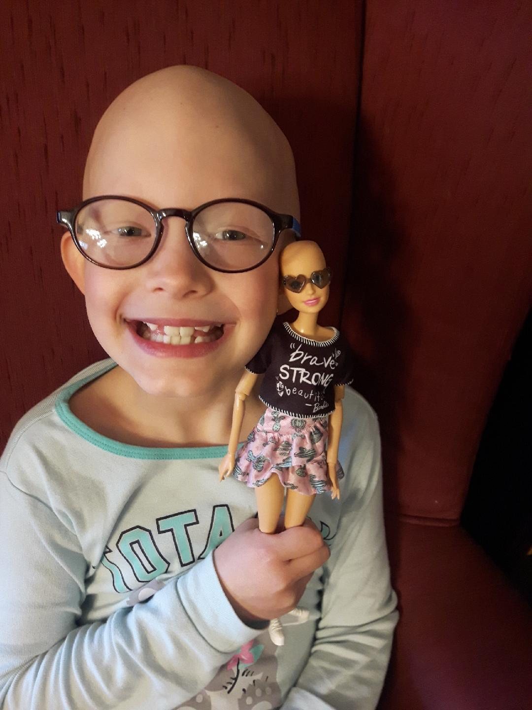 A smiling child holds her Brave Barbie doll