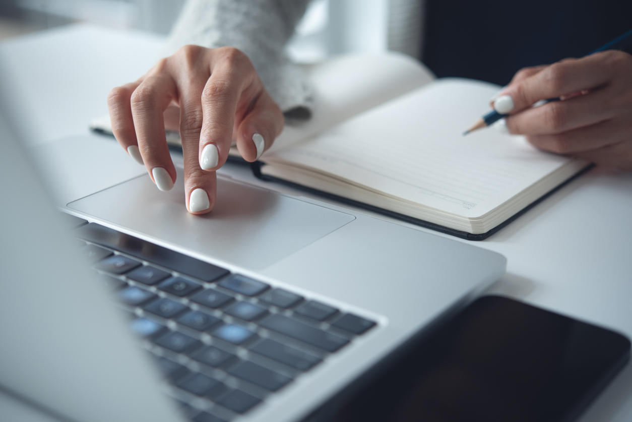 A person types on a laptop beside an open notebook