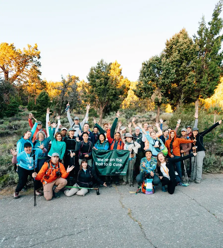 Ultimate Hike participants cheering with arms raised behind a banner reading We are on the trail to a cure