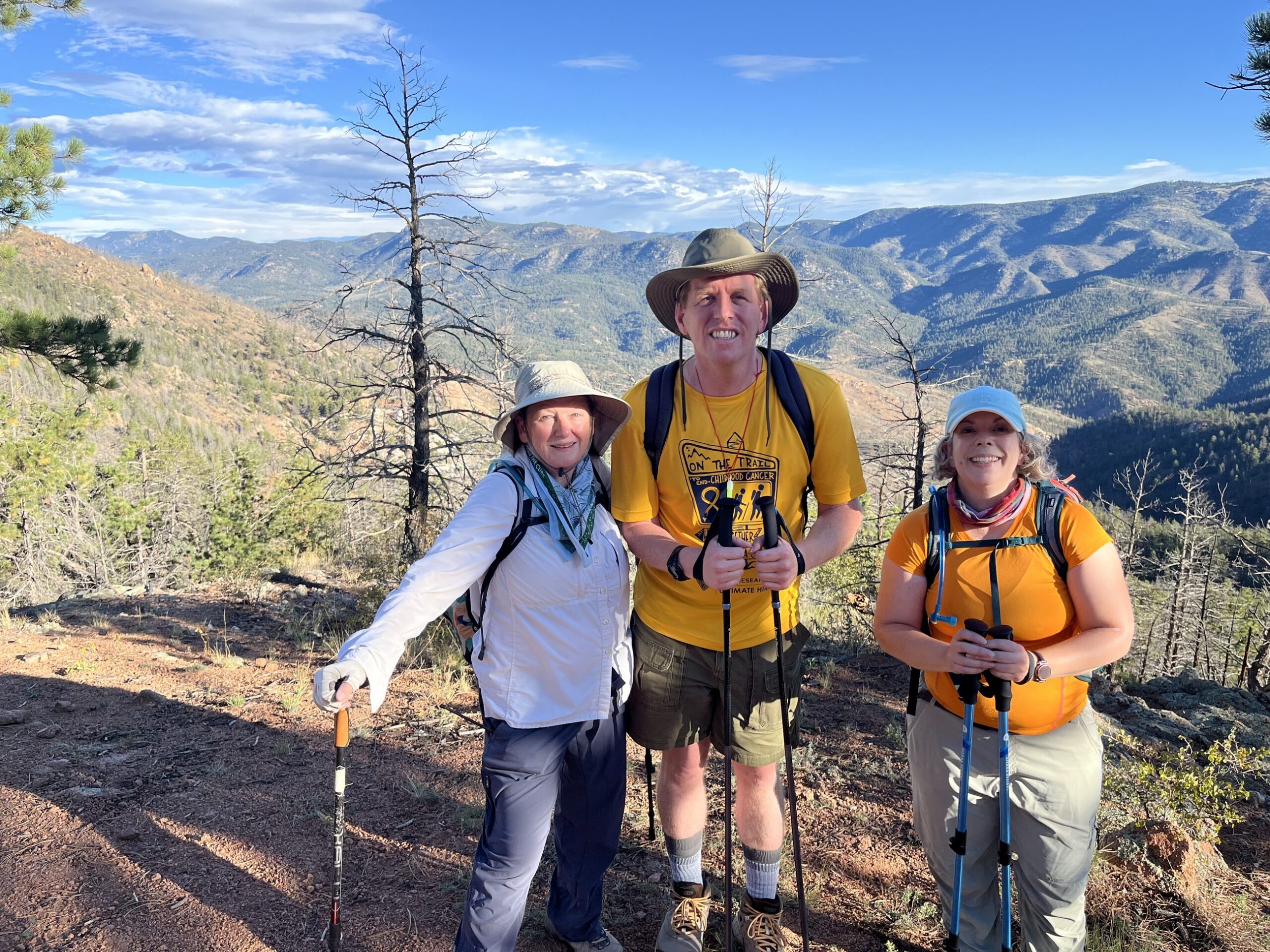 Three Ultimate Hike participants with trekking poles on a Colorado mountain ridge