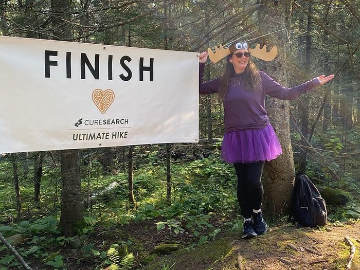 A hiker in a purple tutu celebrating at the FINISH banner