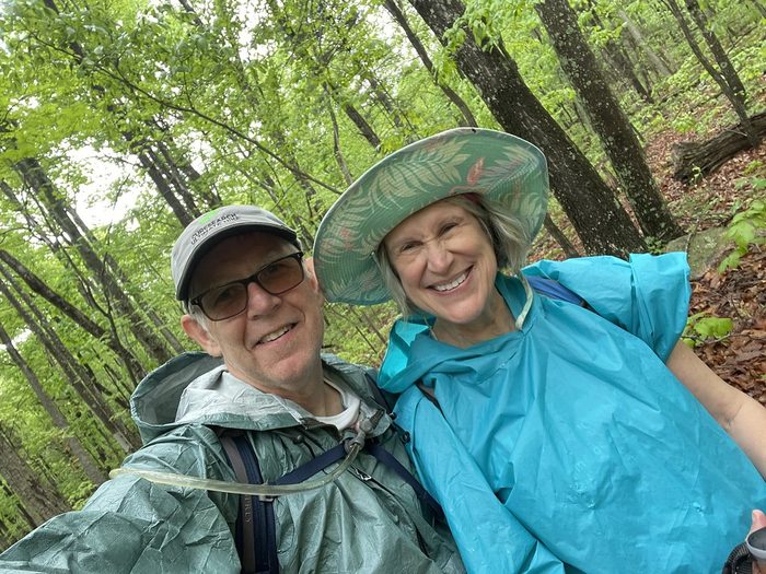 Two hikers smiling in rain ponchos on a wooded trail