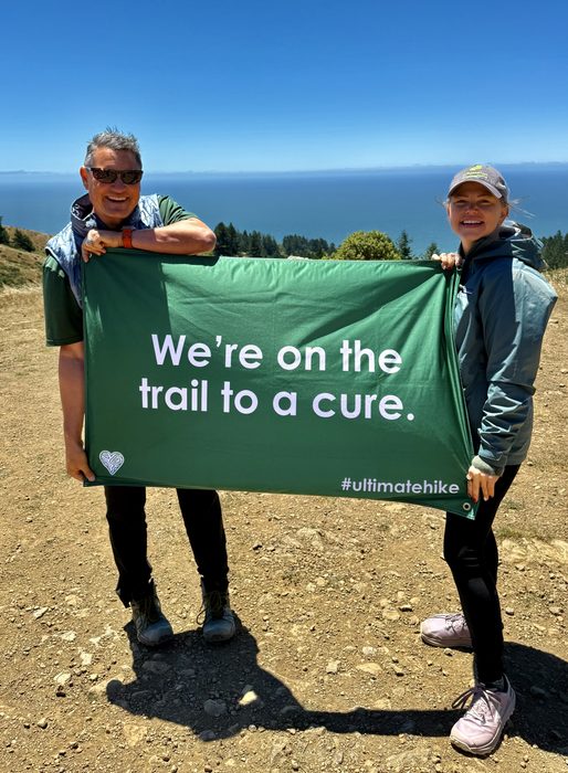 Hikers holding a We are on the trail to a cure banner above the ocean